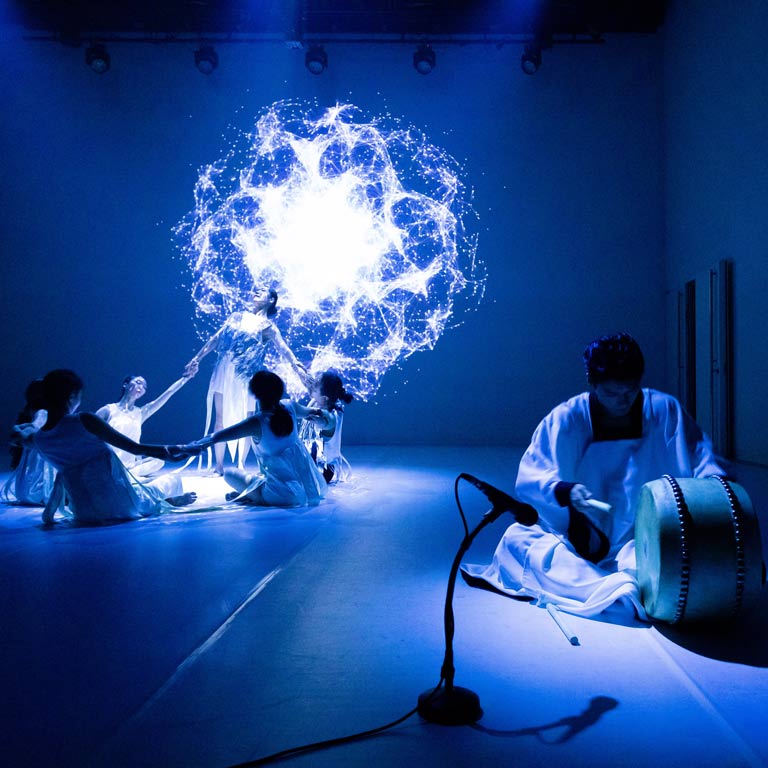 A group of people dance around a white orb above them.