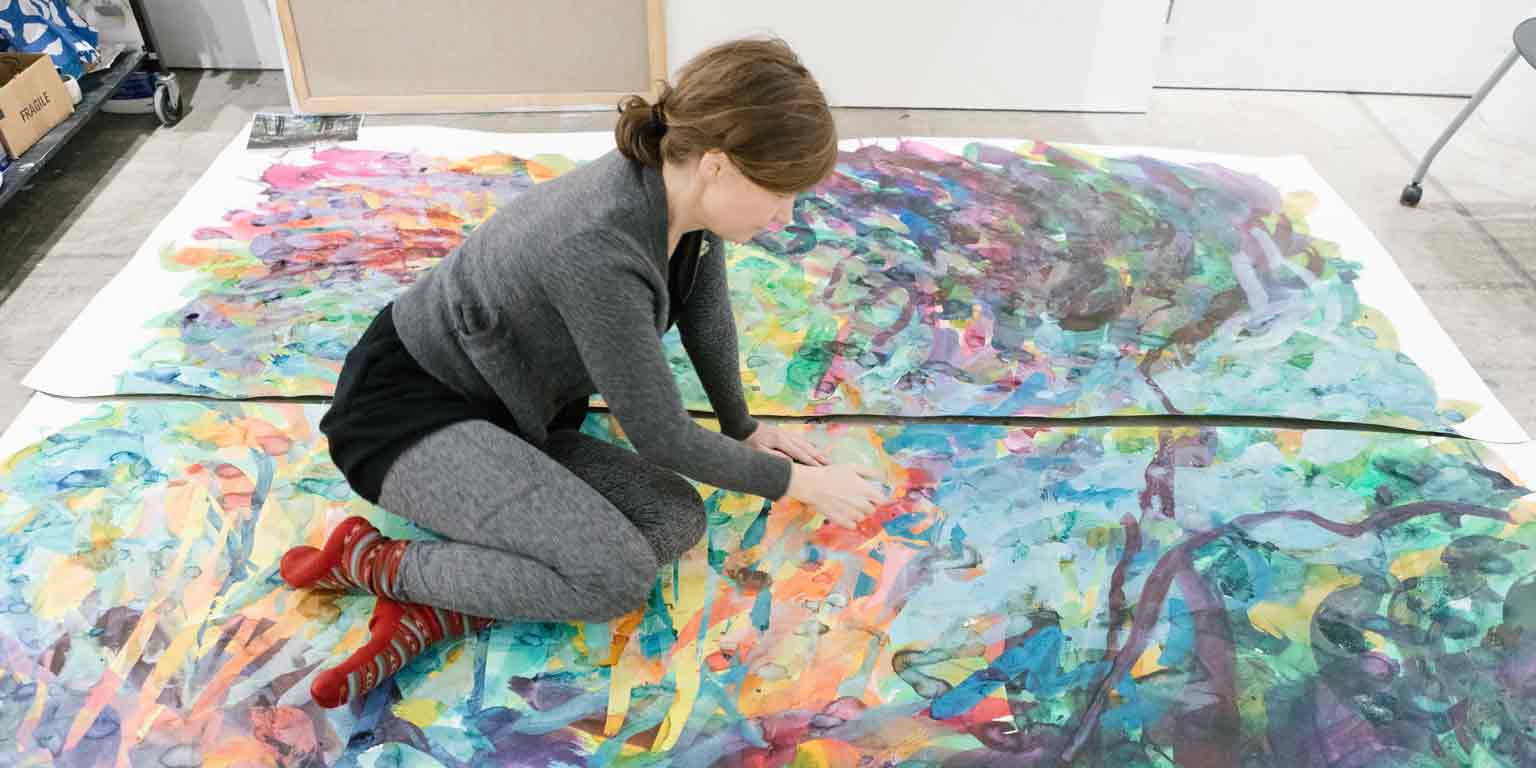 A person paints a large artwork on the ground. 