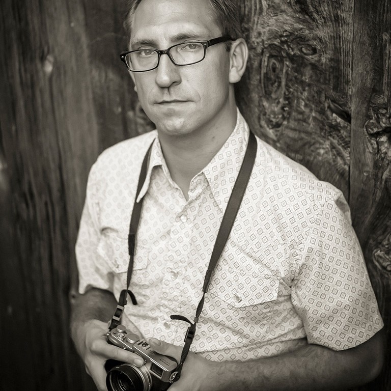 A man holding a camera looks at the camera.