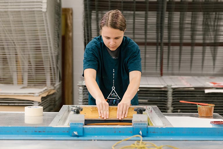 A person works at a screen-printing table.