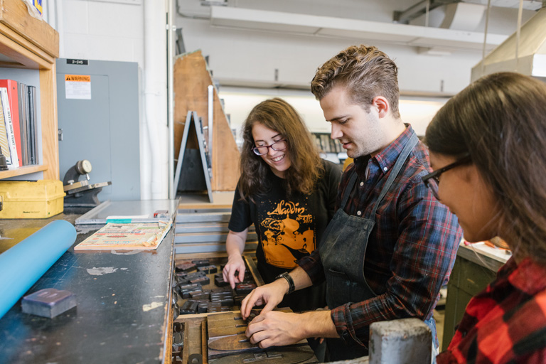 Three students look at a drawer of wood type.
