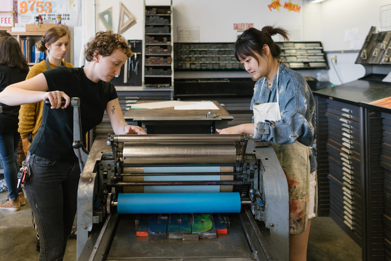 Two students printing artwork using a letterpress.