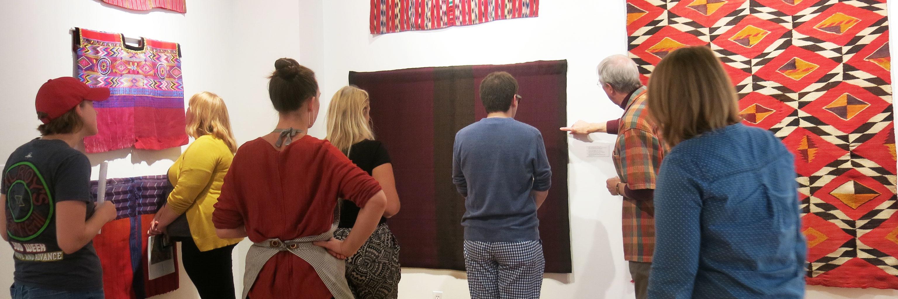 People stand looking at textiles on a wall.