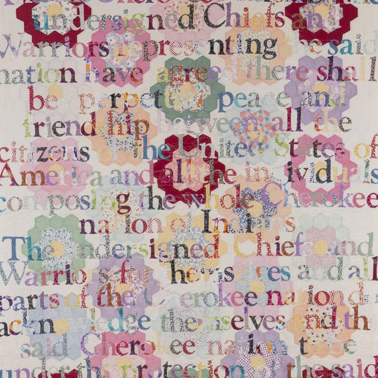 A colorful quilted artwork with phrases appliquéd on top. 