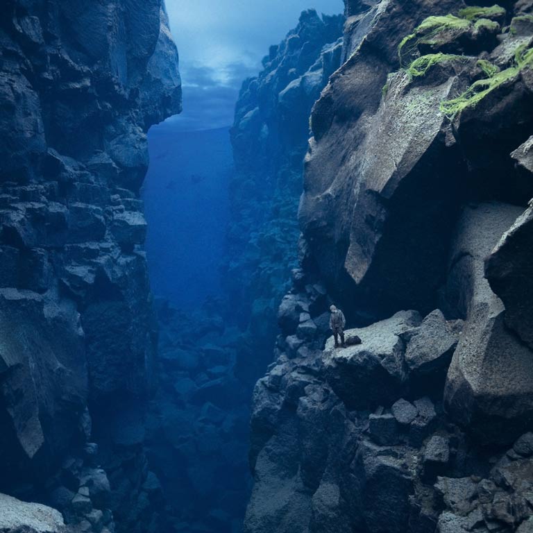 A person stands at the edge of an underwater cliff in a large blue cavern.