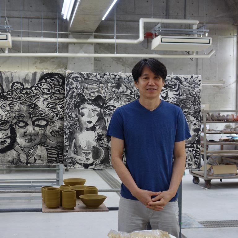 An artist standing in front of a large black and white artwork in their studio.
