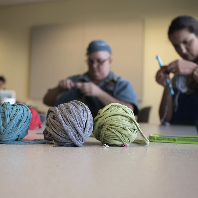 Balls of yarn and people crocheting with large hooks.