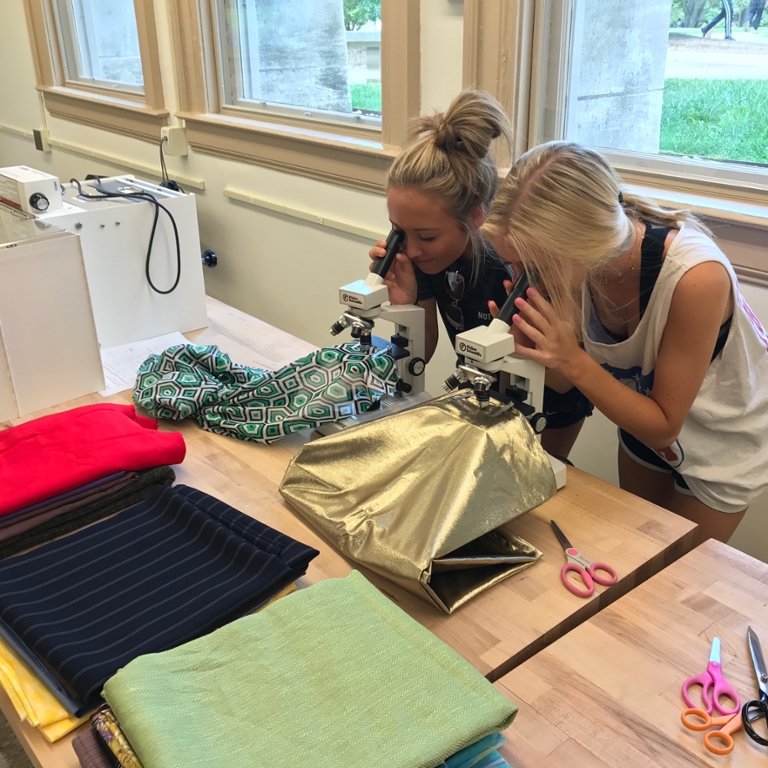 People look at fabric through a microscope.