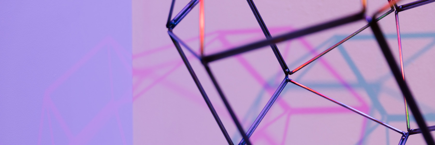 A geometric sculpture hangs against a purple-lit wall.