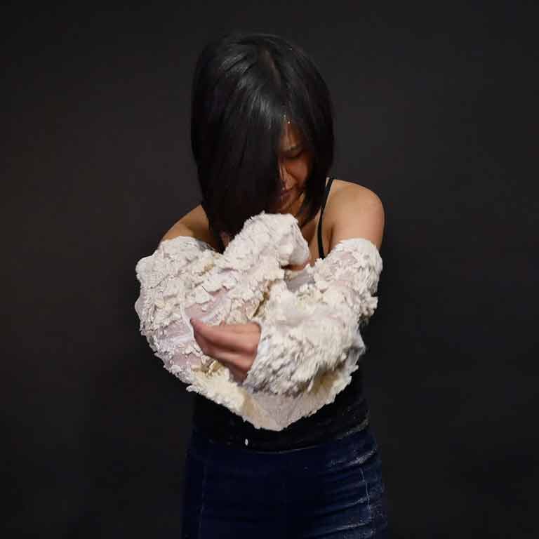 A still capture of a person putting on a white textured shirt. 