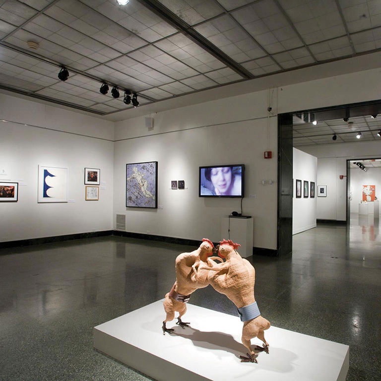 Sculpture of fighting roosters in a gallery.