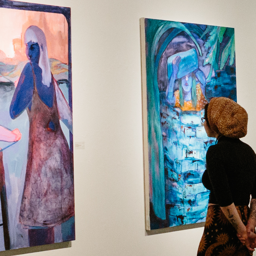 A person looks at paintings in a gallery.