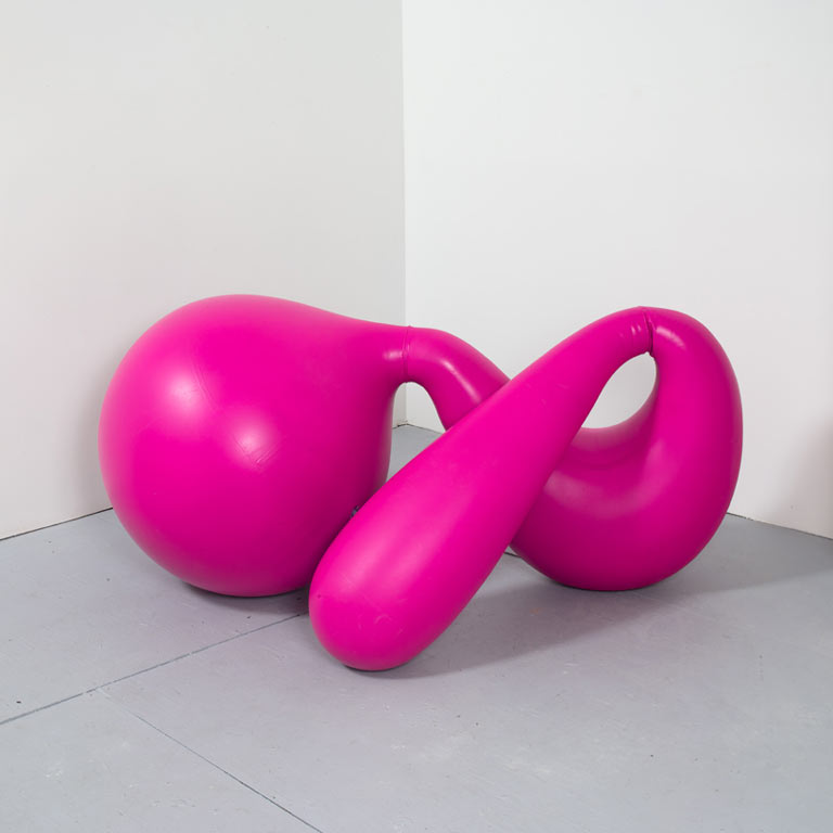 A bright pink sculpture in a gray gallery. 