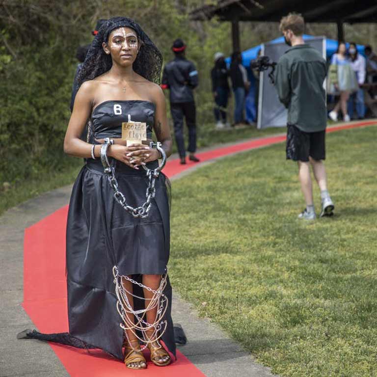 A model walks down an outdoor runway wearing a black gown designed by a student at the Eskenazi School.