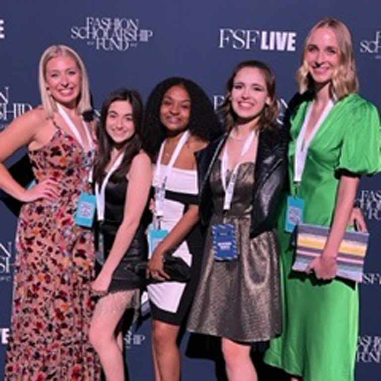 Five students in front of a photo op background for the the Fashion Scholarship Awards Gala. 