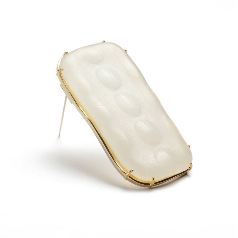 A gold brooch in the shape of a rounded rectangle. The object set in the brooch is a pearly white color. 