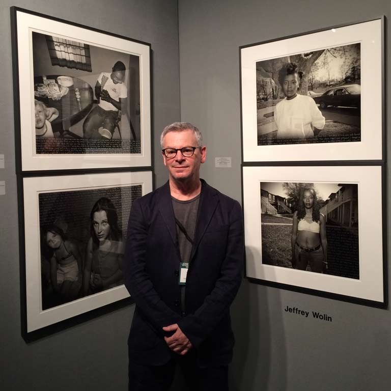 A person stands in front of framed photographs on a wall.