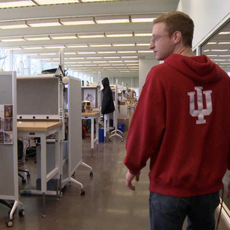A person in an IU sweatshirt walks down a hall with desks.