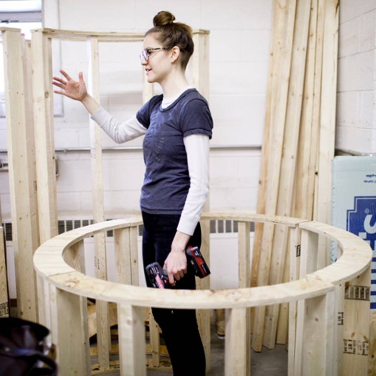 A person with a power tool stands in side a wooden circle