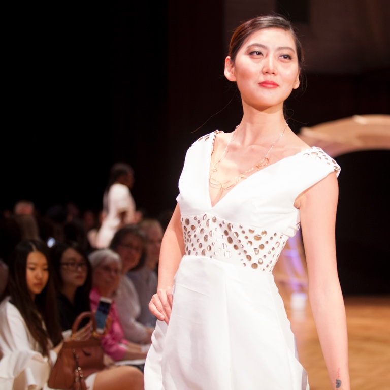 A person wearing white walks a runway.