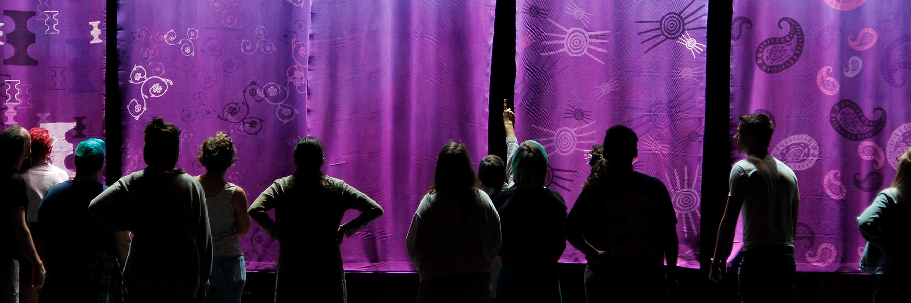 People look at purple artwork on a dark wall.